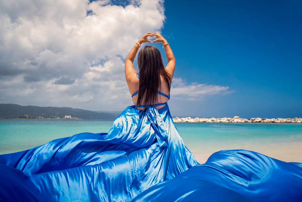 Guest in a blue flying dress making a heart above her head beside the Caribbean Sea