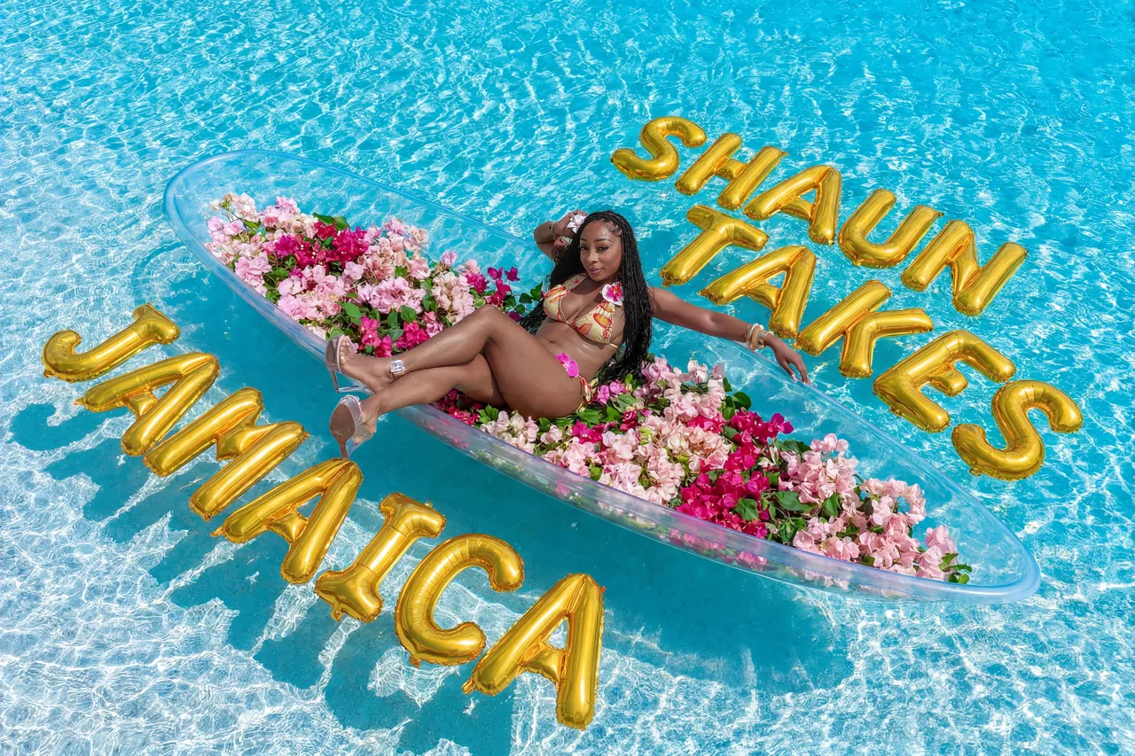 Guest reclining in a clear kayak filled with pink flowers and surrounded by custom gold celebration balloons