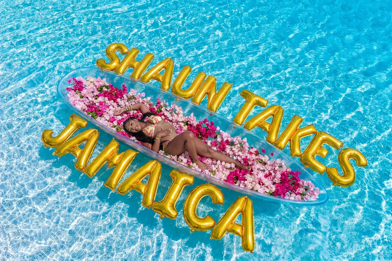 Guest posing in a flower-filled clear kayak with large gold celebration letters over turquoise water