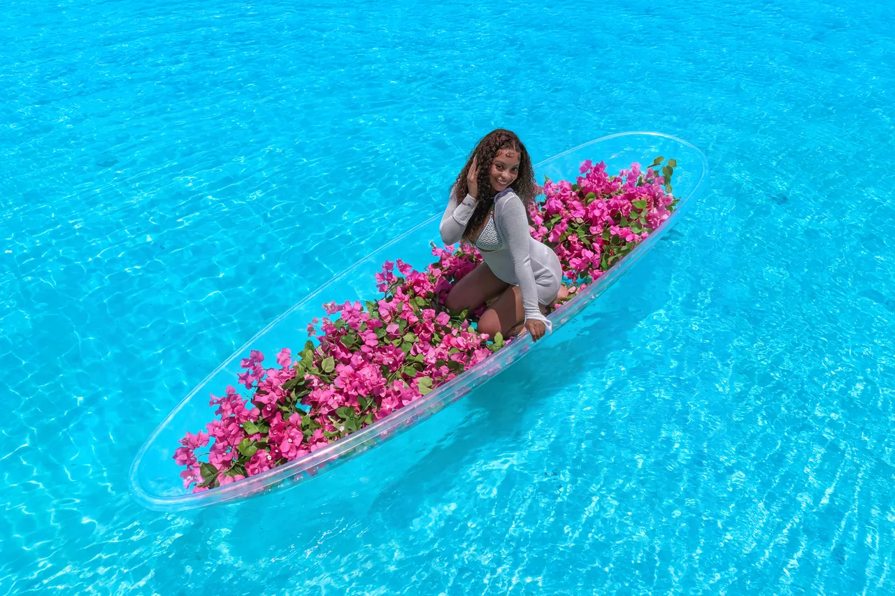 Guest sitting in a clear kayak filled with pink flowers over vivid Caribbean water