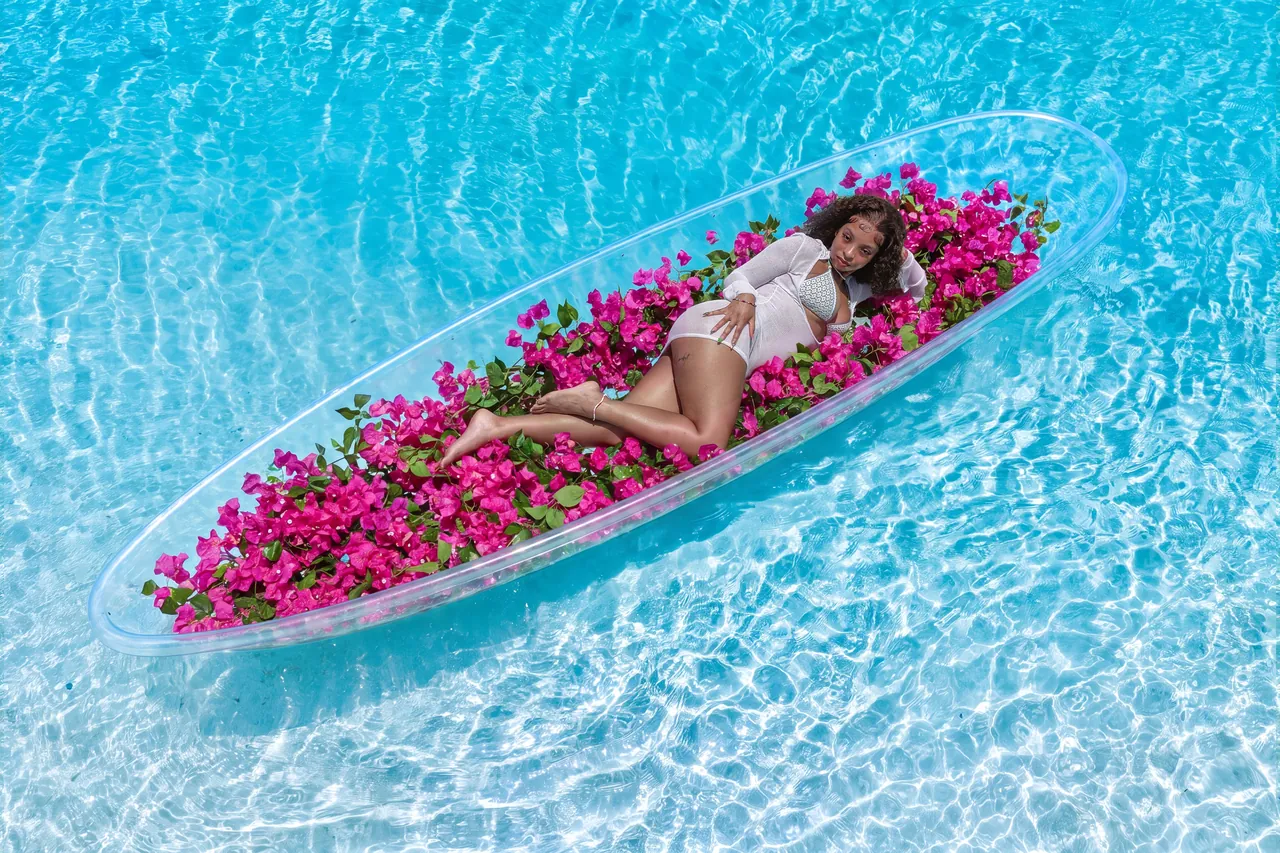 Guest reclining in a clear kayak filled with pink flowers over rippled blue water