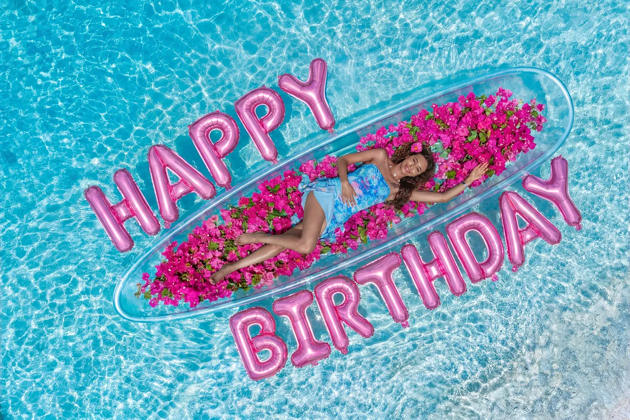 Pink birthday balloons frame a guest reclining in a clear kayak filled with pink flowers
