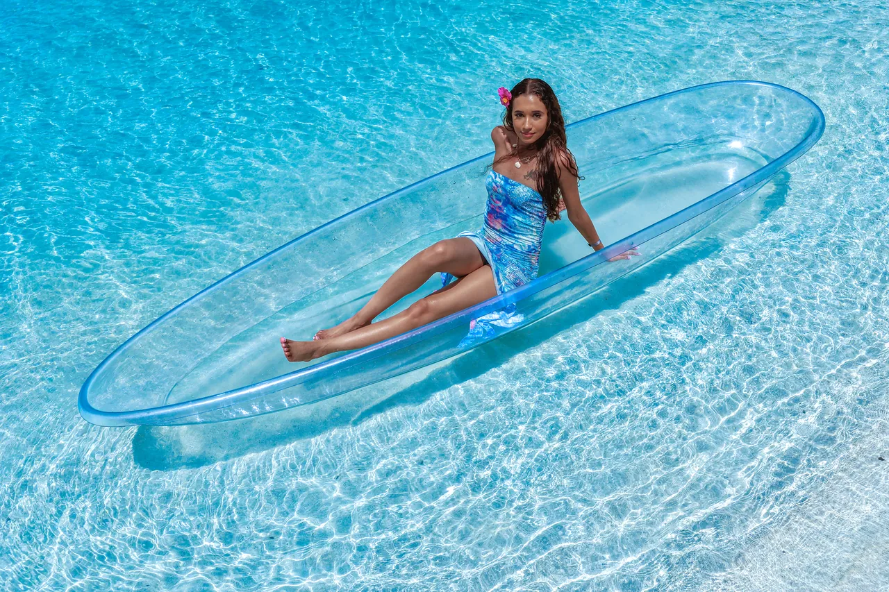 Guest reclining in a clear kayak above pale, rippled Caribbean water