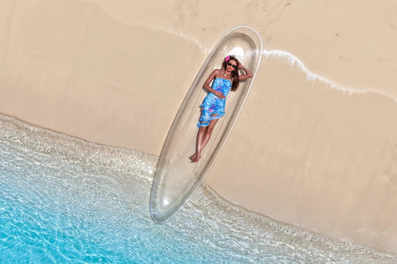 Aerial view of a guest in a clear kayak floating beside the sandy shoreline