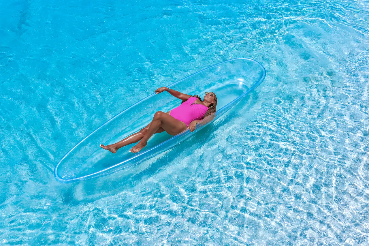 Guest in bright pink reclining in a clear kayak over turquoise water