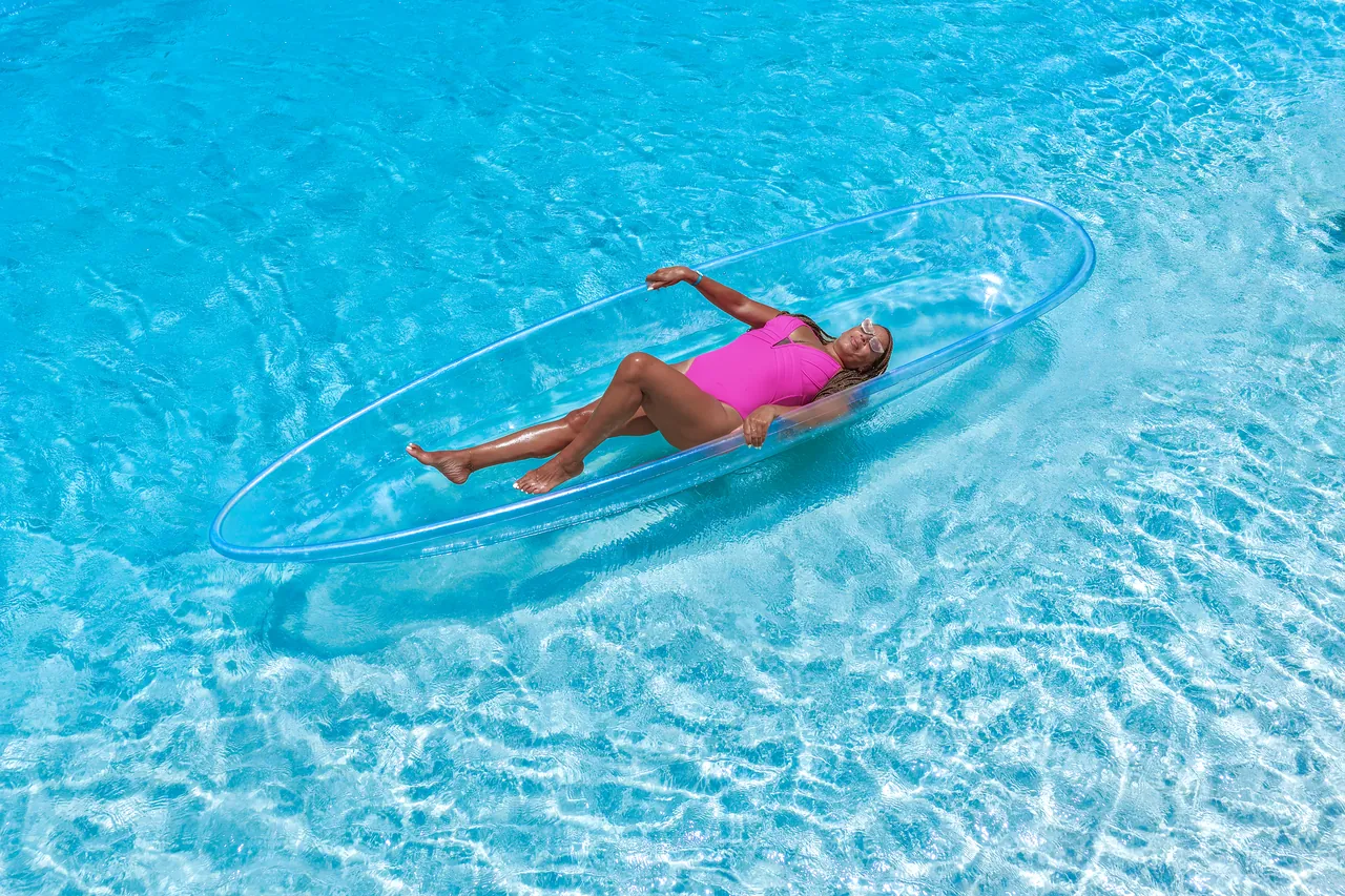 Aerial portrait of a guest in pink floating in a clear kayak over textured blue water