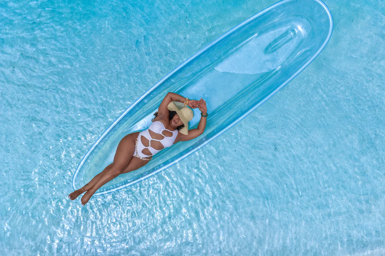 Guest in white reclining in a clear kayak over softly textured blue water