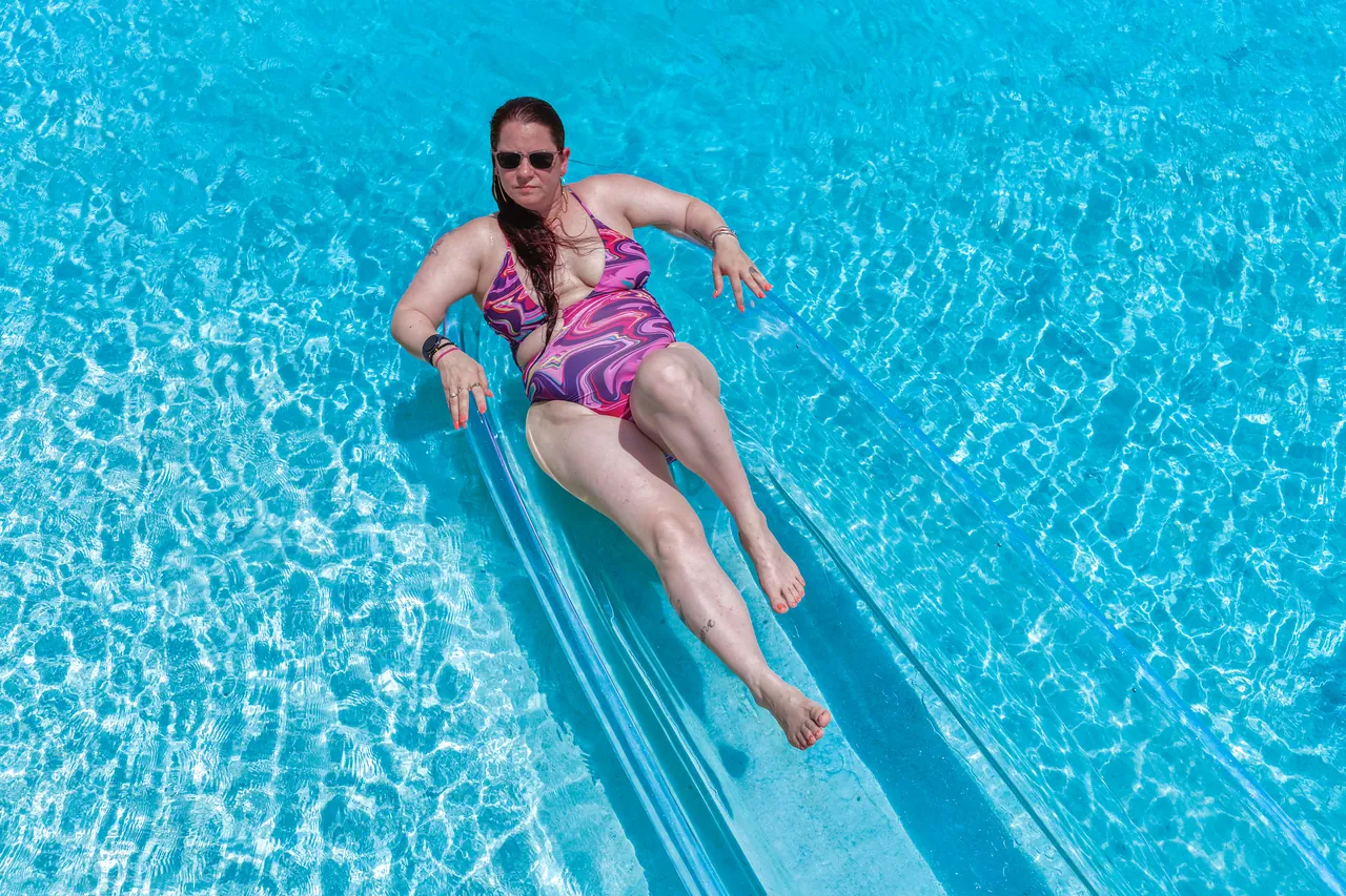Guest wearing sunglasses reclining in a clear kayak over blue water