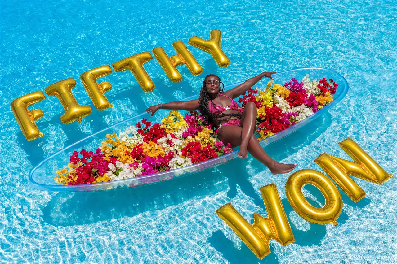 Guest in a multicolour flower-filled kayak surrounded by large custom gold balloons