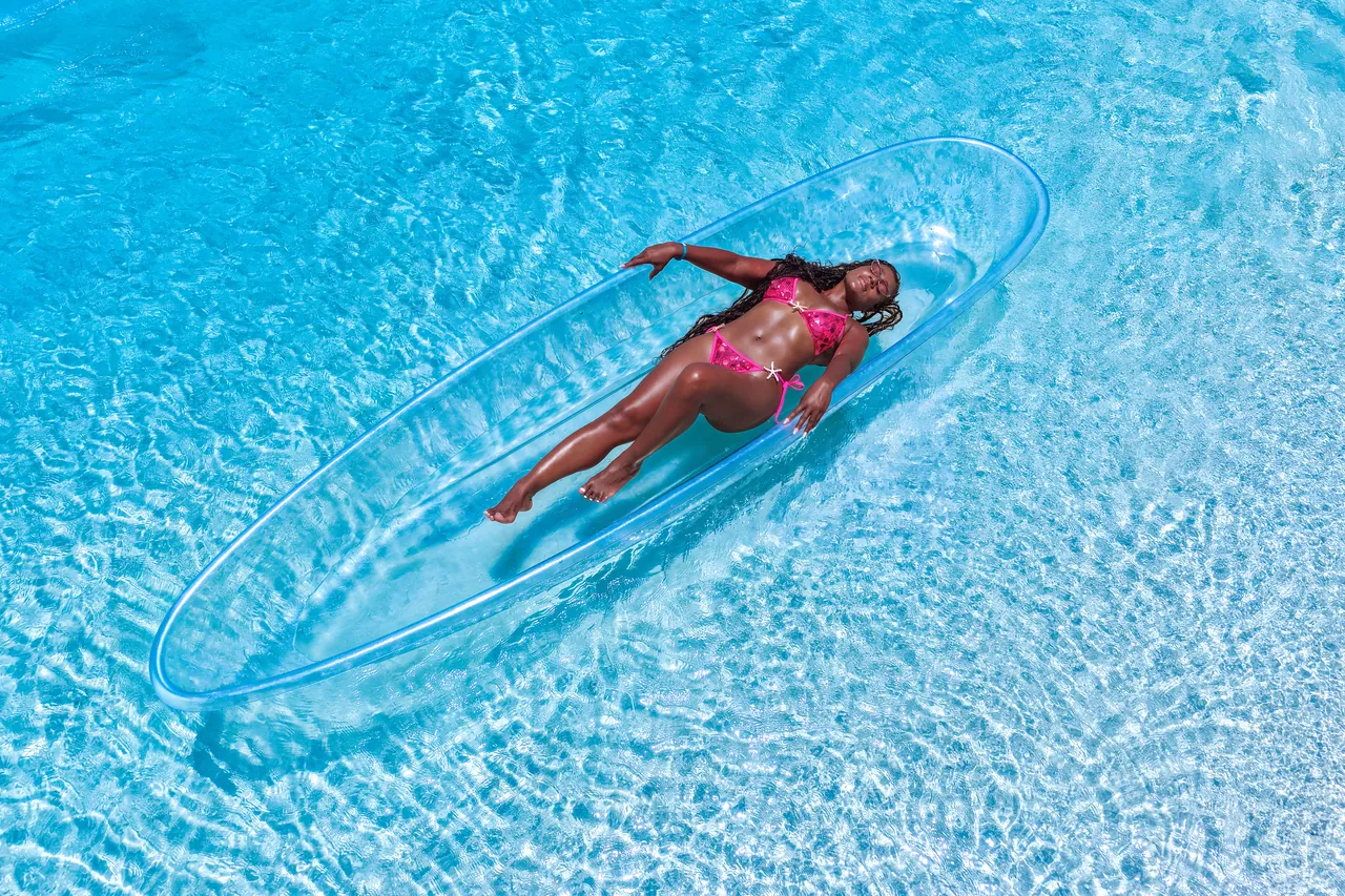 Guest in a pink swimsuit reclining in a clear kayak over vivid turquoise water